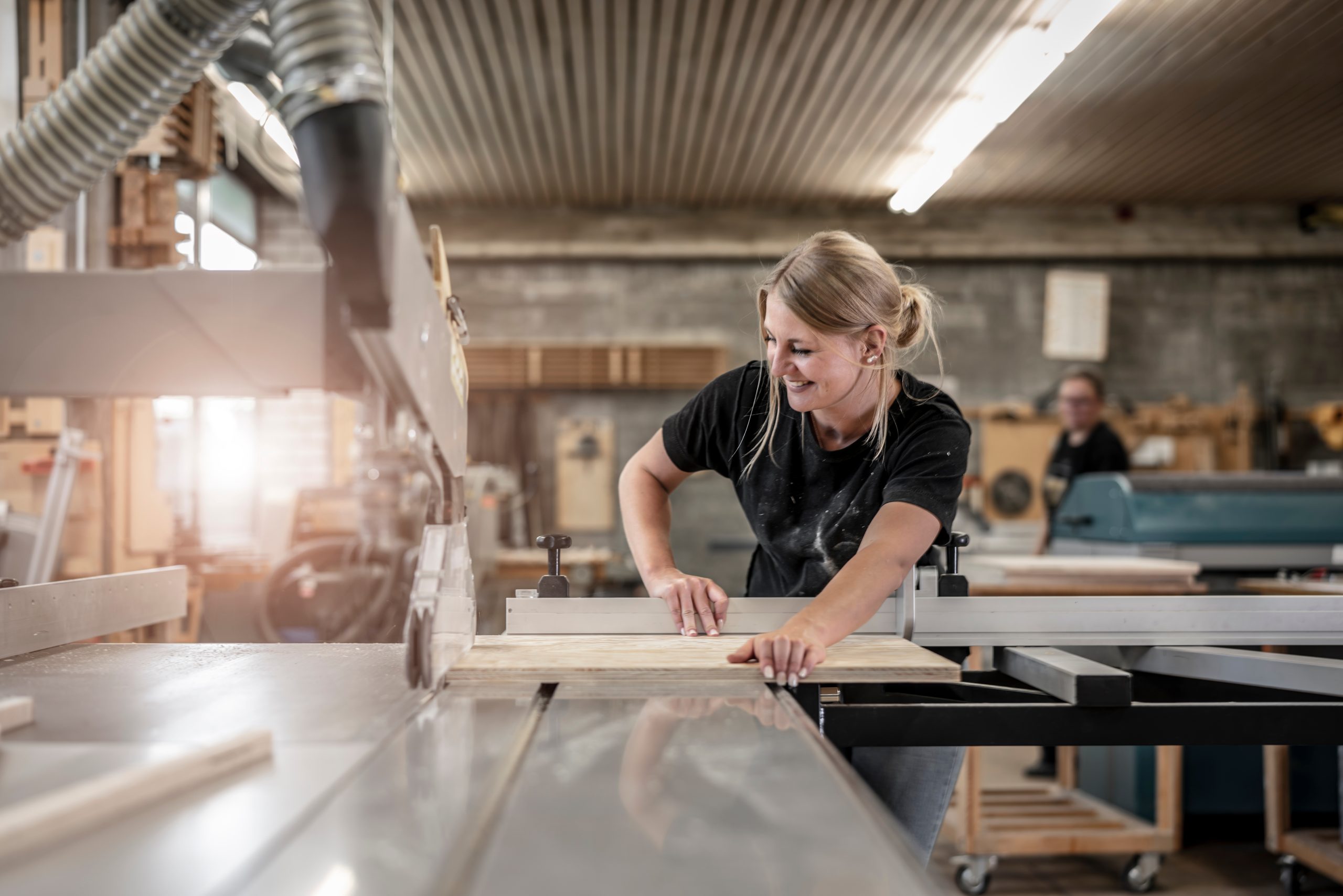 Junge Schreinerin sägt an der Kreissäge eine Holzplatte